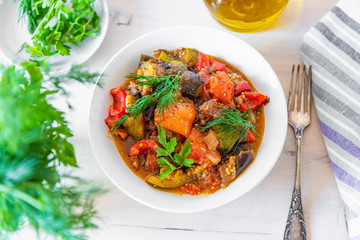 Vegetable stew in a plate on a light rustic wooden background