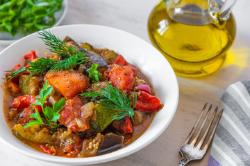 Vegetable stew in a plate on a light rustic wooden background