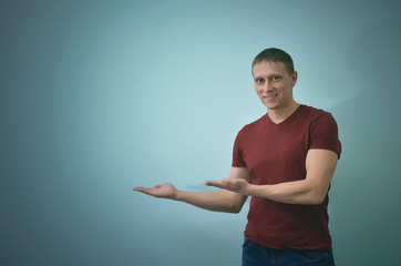 Young smiling man is showing on the copy space near him isolated on blue background.