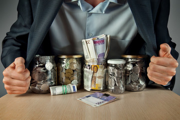 A man in a suit conserved money in glass jars. The concept is the storage of money, stocks at difficult times. Conserve money instead of vegetables.
