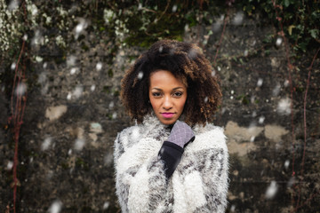 Stylish afro hair woman winter portrait under the snow. Female wearing warm clothes and gloves.
