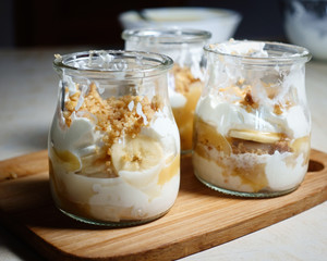 Caramel dessert Banoffi pie in glass jars on a wooden board