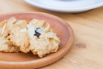two pieces of cashew cookies on wooden dish with blurred white coffee cup on the background