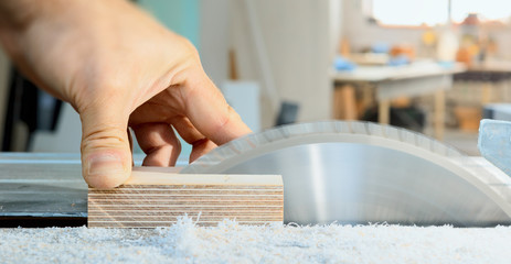 The carpenter cuts the wooden part on the saw. A sharp saw blade is going to cut of a workers thumb. Risk at workplace.