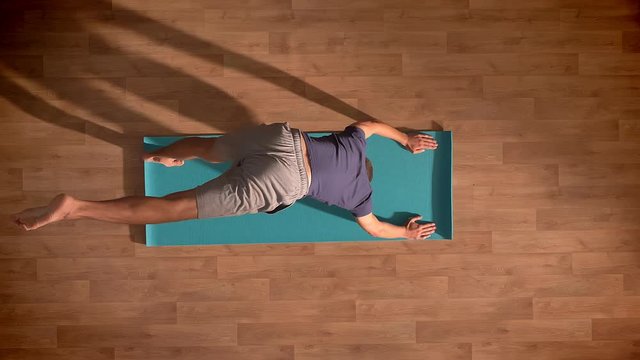 Top down shot, caucasian man inn practising yoga on blue mat, stretching his body relaxed on wooden floor