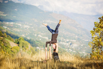 Giovane coppia pratica acroyoga e yoga all'aperto in montagna al parco