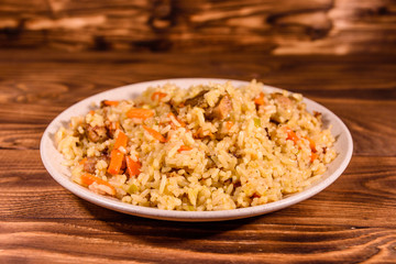 Ceramic plate with pilaf on wooden table