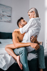 Obraz premium passionate young man sitting on bed with seductive girlfriend on top