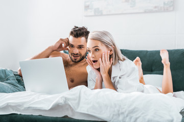 shocked young couple using laptop together in bedroom