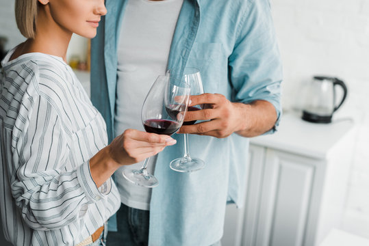 cropped image of young couple clinking with wineglasses in kitchen