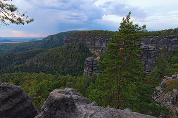 Fototapeta na wymiar Picturesque panorama with typical rocky peaks, ancient forest under cloudy sky. Bohemian Switzerland National Park. Famous touristic place and travel destination in Europe. Czech Republic