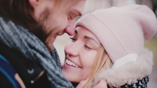 Close-up view of happy smiling young European romantic couple stand close together and talking outside on a cold day.