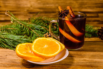 Cup of mulled wine with cinnamon, sliced orange and fir tree branches on wooden table