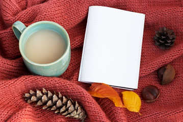 cup of coffee with an autumn leaf, notepad and cones on a knitted sweater close-up, top view, copy space