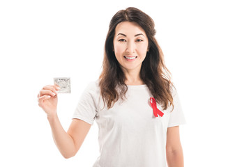 happy adult asian woman with aids awareness red ribbon on t-shirt holding condom isolated on white