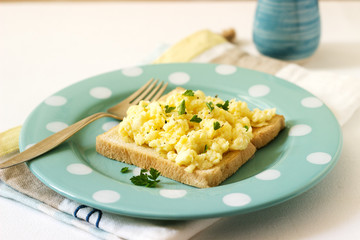 Simple classic breakfast of bread toast and scrambled eggs with parsley.