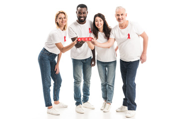 Obraz premium smiling multiethnic people in blank white t-shirts with aids awareness red ribbons holding blocks with AIDS lettering isolated on white