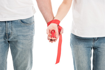 cropped shot of couple holding hands tied with red ribbon isolated on white, aids awareness day concept