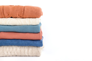 Stack of warm orange and blue pastel sweaters isolated on white.