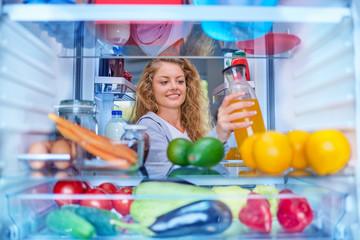 Woman standing in front of fridge full of groceries and taking juice. Picture taken from inside of fridge.
