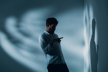 Man with schizophrenia standing alone in a room pointing at his shadow on the wall, real photo with...