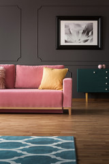 Fancy dresser with golden elements and a velvet pink sofa on hardwood floor in a vintage living room interior with gray walls. Real photo.