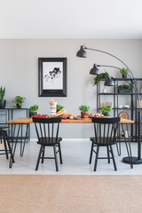 Brown carpet in front of black chairs and wooden table with food in grey dining room interior. Real photo