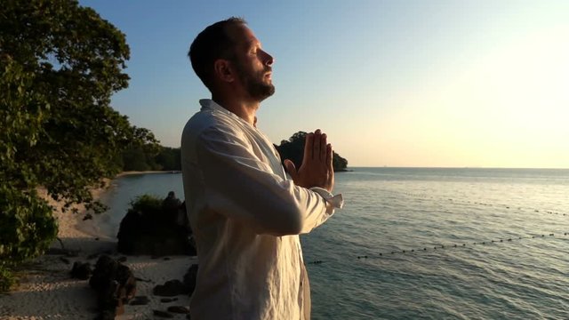 Young handsome man meditating by the sea during sunset, slow motion