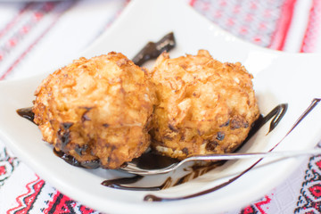 Two balls of fried ice cream poured with chocolate syrup on a white plate.