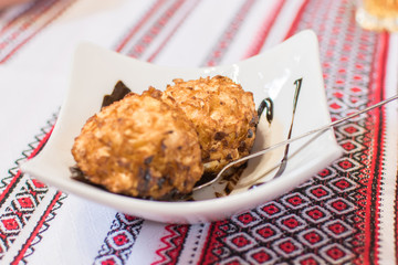 Two balls of fried ice cream poured with chocolate syrup on a white plate.