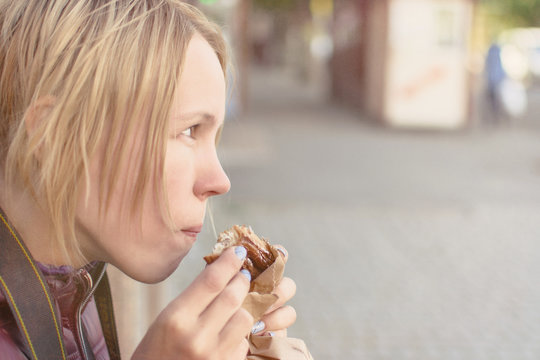 Attractive woman eats croissant on the street.