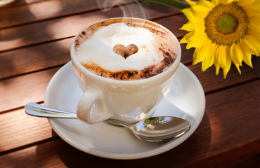 Dampfender aromatischer Kaffee mit Schaum auf einem Holztisch mit Sonnenblume