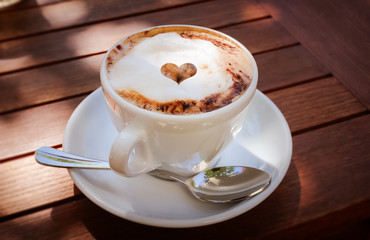 Dampfender Kaffee mit Schaum auf einem Holztisch im Cafe draussen in der Sonne