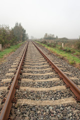 Rusty seemingly endless single track train tracks through a rural Dutch area with early morning fog