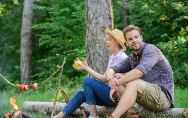 Naklejka na ściany i meble Idyllic picnic date. Pleasant smell of roasted food makes picnic atmosphere perfect. Couple in love relaxing sit on log having snacks. Family enjoy weekend in nature. Picnic roasting food over fire