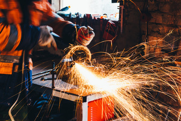 Worker cutting metal with grinder in his workshop. Sparks while grinding iron