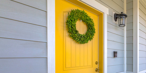 Wreath on yellow front door and a lamp on a wall © Jason