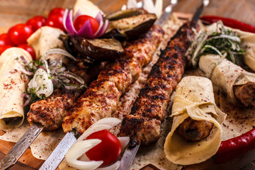 Kebab on skewers on a wooden tray with cherry tomatoes and hot pepper