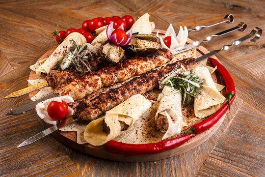 Kebab on skewers on a wooden tray with cherry tomatoes and hot pepper