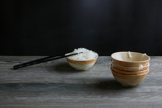 Bowl of cooked white rice and japanese chopsticks place on wooden table and empty bowl stack. consumer more eating concept..