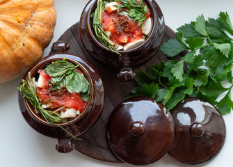 Top view image of two clay pots with vegetables, greenery and seasoning; healthy traditional food in old crockery on wooden board; bright colors of fresh season food rich in vitamins from the garden