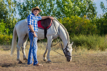 The man in a shirt and a hat walks with a white horse