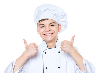 Handsome teen boy wearing chef uniform making thumbs up gesture. Portrait of a happy cute male child cook, isolated on white background. Food and cooking concept.