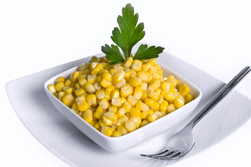 Bowl full of corn, with a sprig of parsley, on white background.