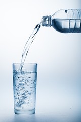 Pouring Water from Bottle into Glass on the Blue Background