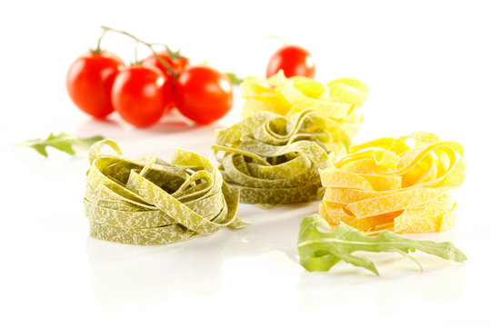 Close-up of spanach, basil tagliatelle pasta, fettuccine nest, rucola, bunch of cherry tomatos on white background