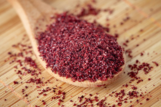 Close up of ground sumac spice powder in wooden spoon