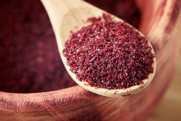 Close up of ground sumac spice powder in wooden spoon