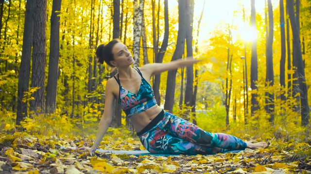 Young beautiful woman doing choreographic exercises in autumn forest. Sunny day, golden autumn