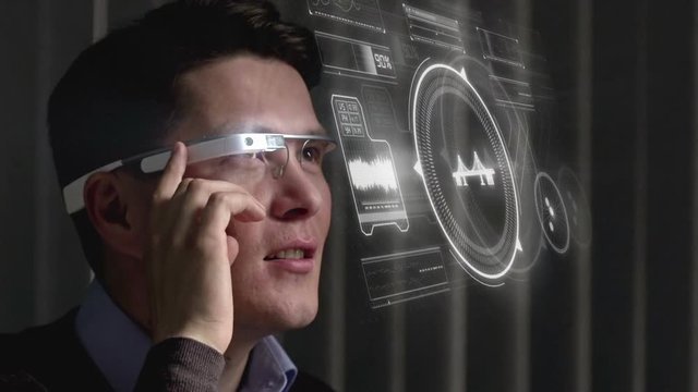 Close up of cheerful Asian man using the touch pad built on the side of smart glasses and looking at virtual interface projected in the air